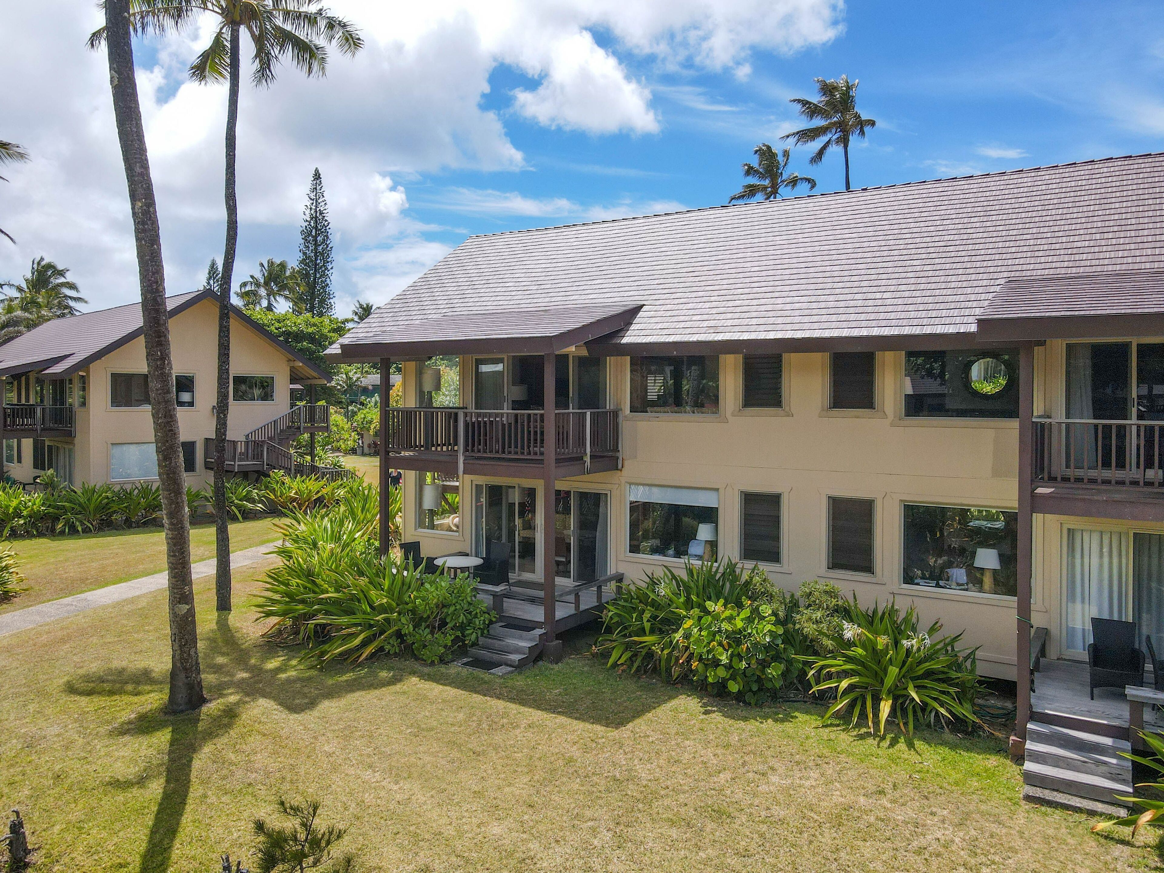 A two-story hotel with a balcony, a covered outdoor seating area, and a well-maintained lawn.