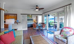 A spacious living area with a dining set, a sofa with colorful cushions, a ceiling fan, and a sliding glass door leading to an outdoor patio. - Hanalei Colony Resort H4 (Hanalei)