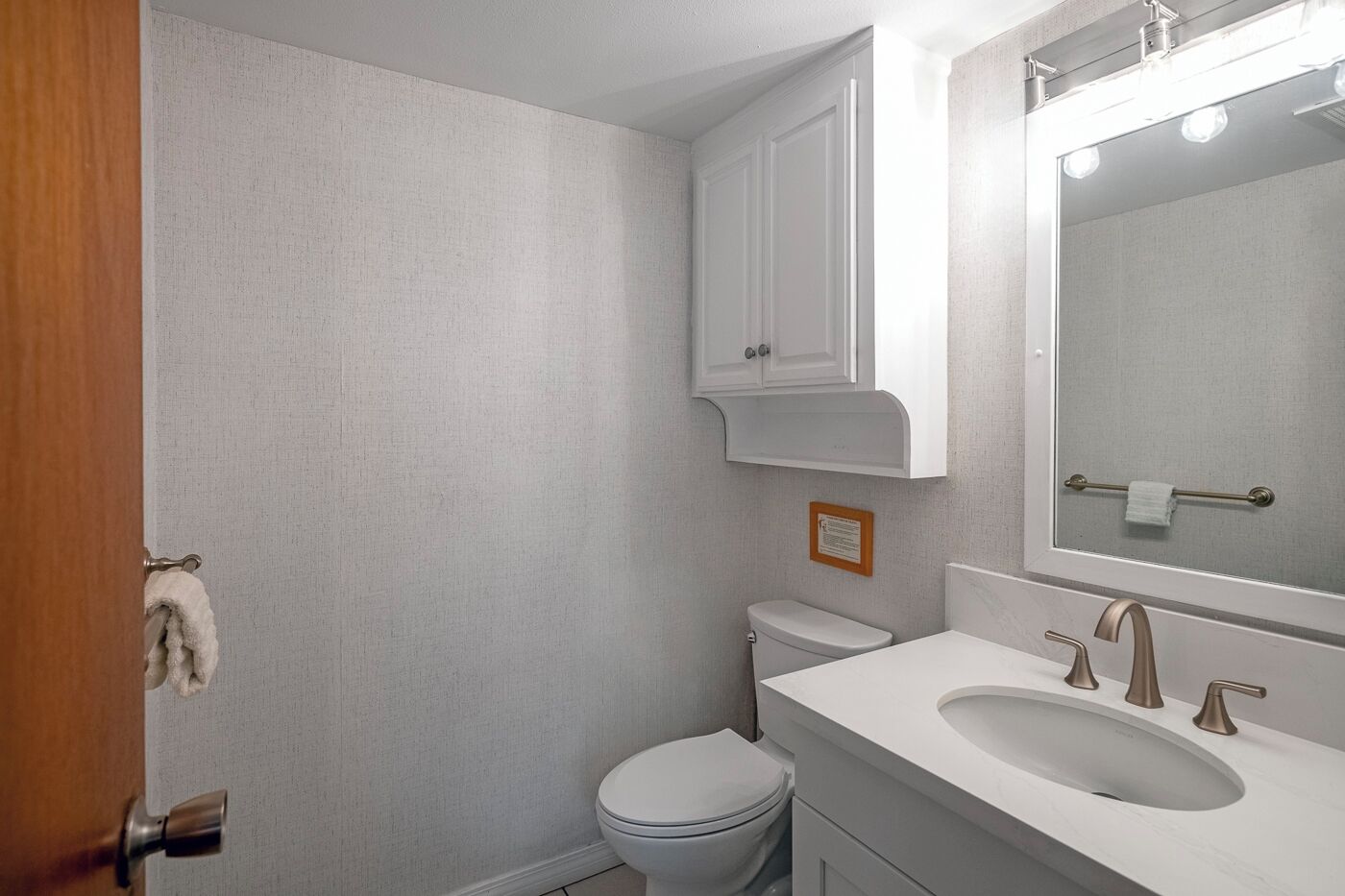 A bathroom with a toilet, sink, mirror, and towel rack.