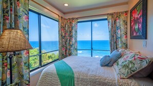 Un dormitorio con una cama grande, cortinas florales y vista al océano.