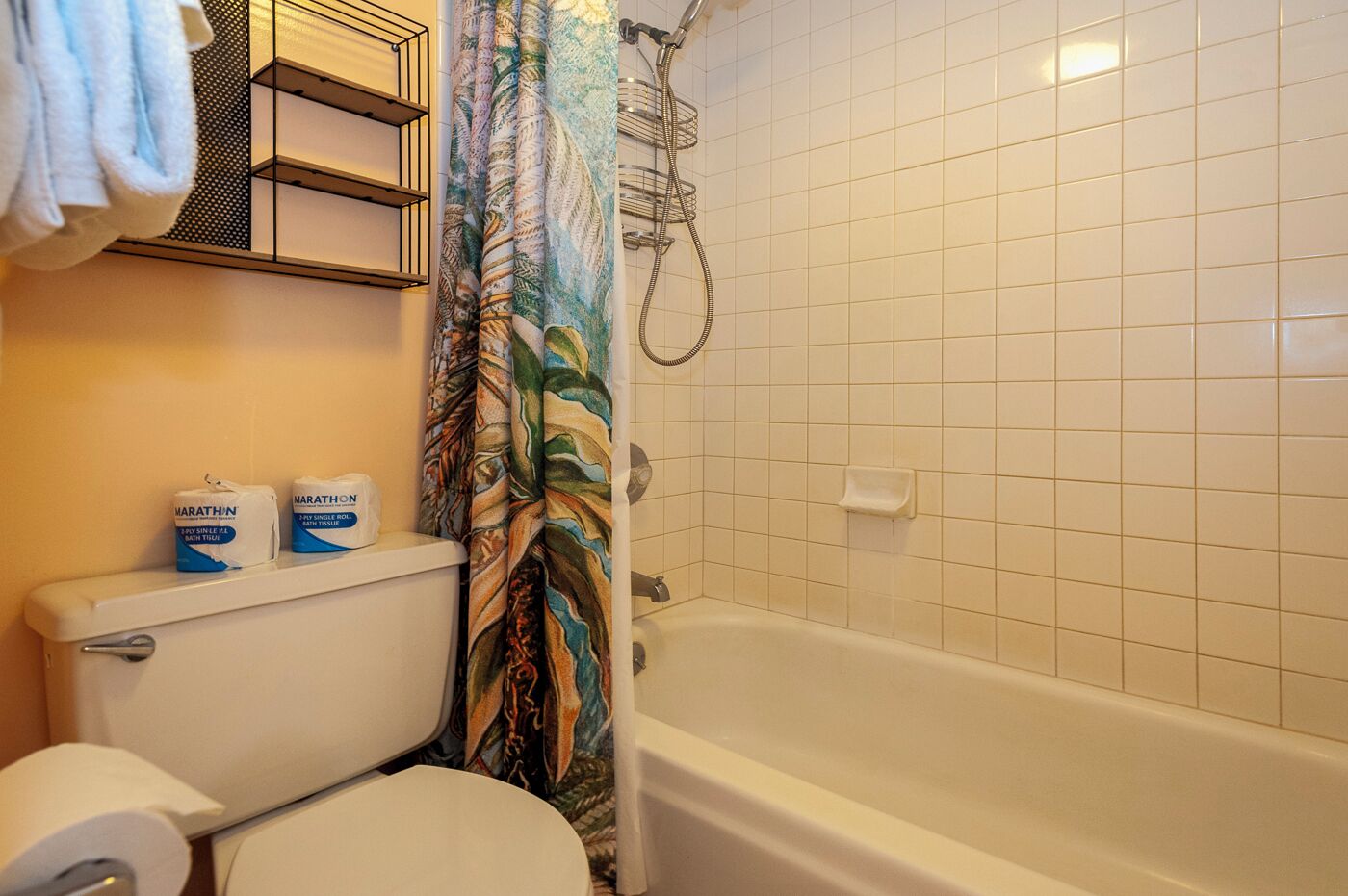 A bathroom with a toilet, a shower with a curtain, and two boxes of toilet paper on the wall.