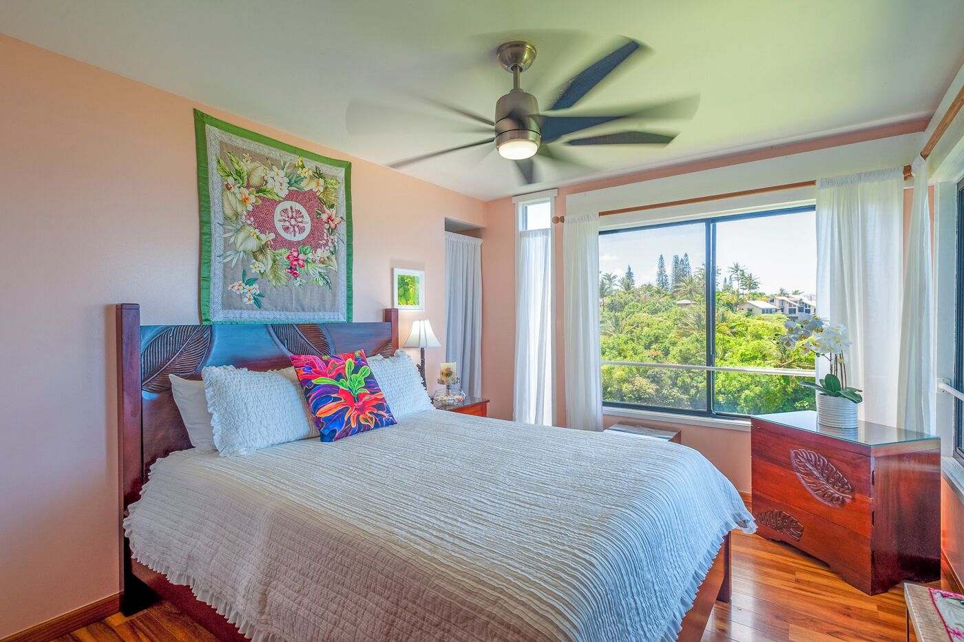 Una camera da letto con un letto grande, una ventola a soffitto, una finestra vista verde e un quadro decorativo sopra il letto.