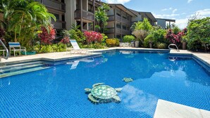 Ein Swimmingpool mit einer Schildkrötenstatue in der Mitte, umgeben von üppiger Bepflanzung und einem mehrstöckigen Gebäude im Hintergrund.