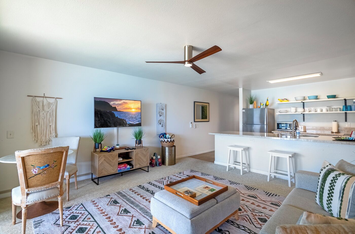A modern living room with a TV, a ceiling fan, a kitchen area with a fridge, and a bar.