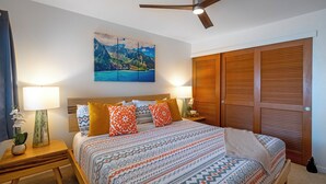 Ein Schlafzimmer mit einem Bett, zwei Nachttischen, einem Schrank, einem Deckenventilator, einem Holzschrank und einem Bild an der Wand.