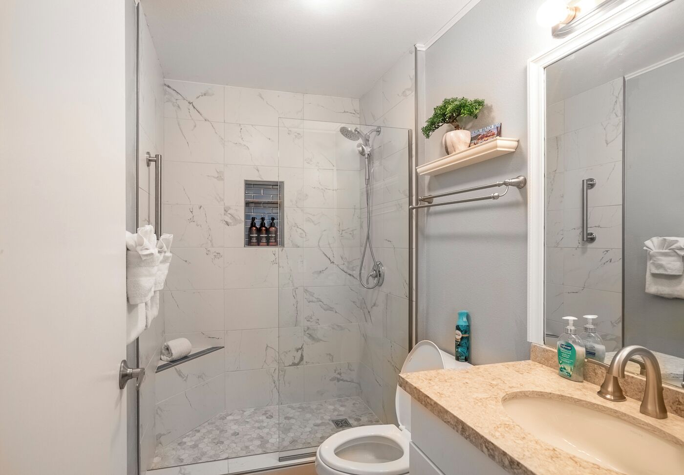 A bathroom with a shower, toilet, sink, and a mirror.
