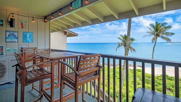 Ein Holztisch und -stühle auf einem Balkon mit Blick auf das Meer und Palmen.