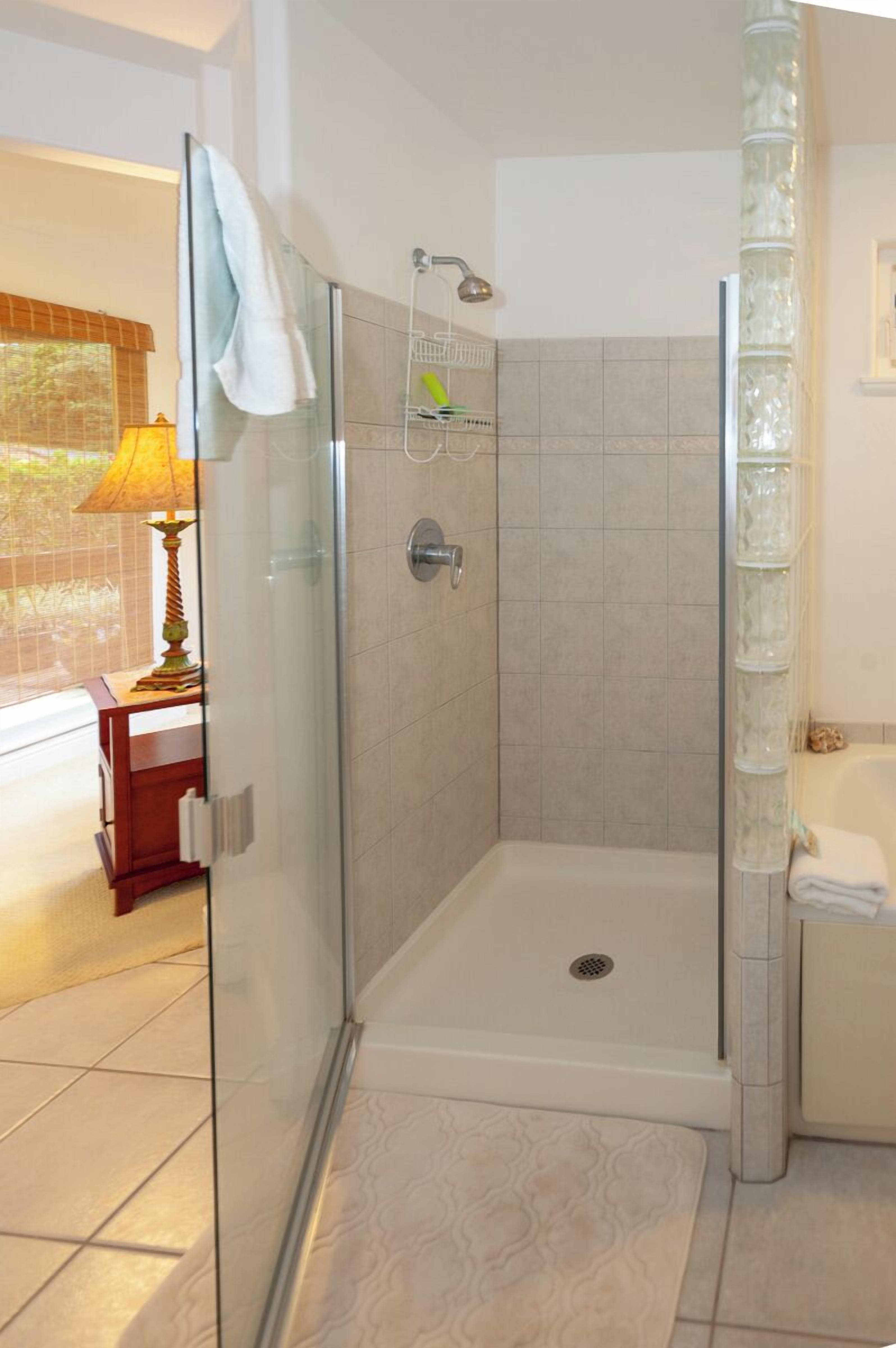 Une douche fermée par des parois de verre, dotée d’un pommeau de douche à main, d’un rideau de douche en verre et d’une serviette blanche accrochée à la porte en verre.