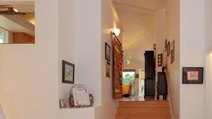 Ein heller, sauberer Flur mit einer Holztreppe zu einem Zimmer. An der Wand befinden sich gerahmte Bilder und ein kleiner Tisch mit einer Blumenvase.