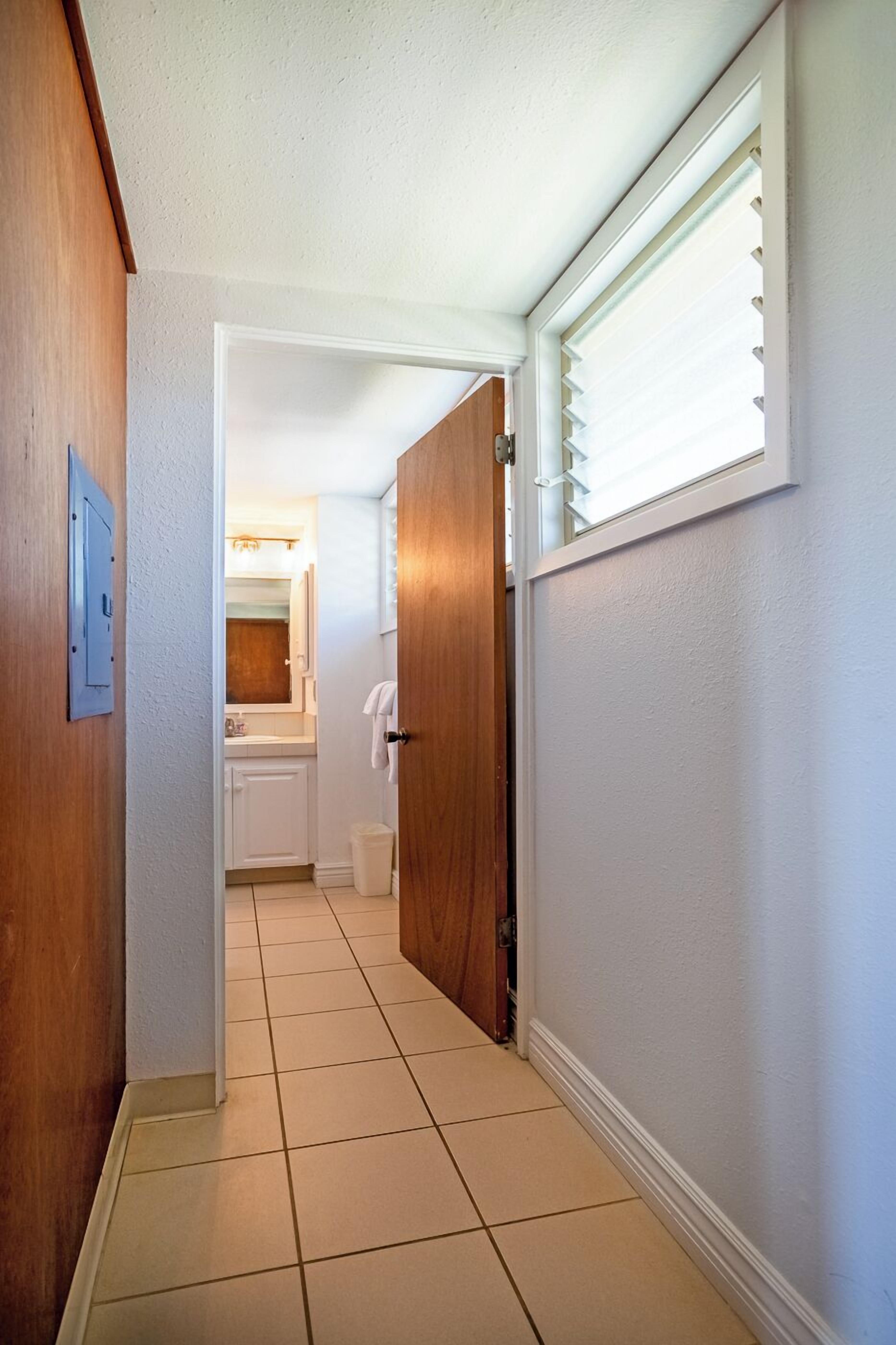 A hallway with a wooden door, a white wall, and a window with blinds.