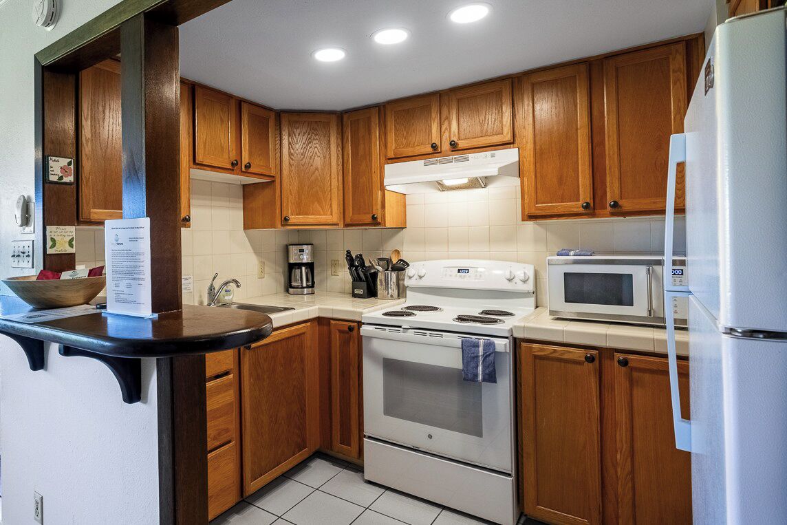 A kitchen with wooden cabinets, a white stove, a microwave, and a refrigerator.