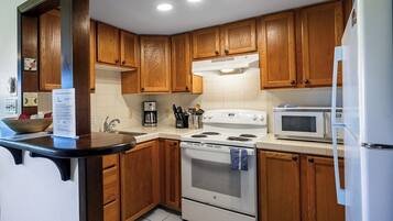 A kitchen with wooden cabinets, a white stove, a microwave, and a refrigerator.