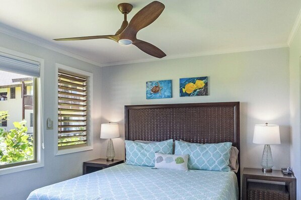 A bedroom with a bed, two wall-mounted paintings, a ceiling fan, and a window with blinds. - Hanalei Colony Resort C2 (Hanalei)
