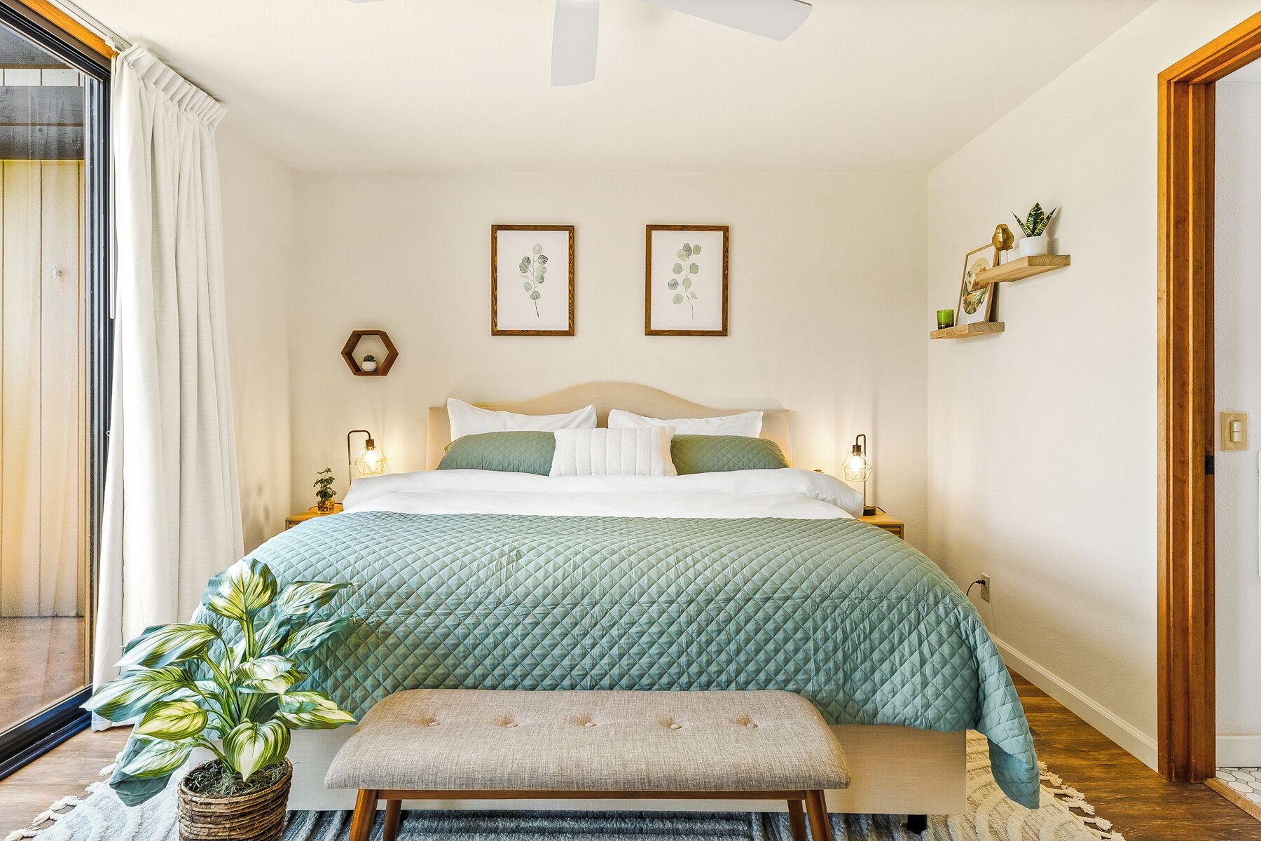 A bedroom with a bed, bedside tables, a bench, a potted plant, and framed pictures on the wall.