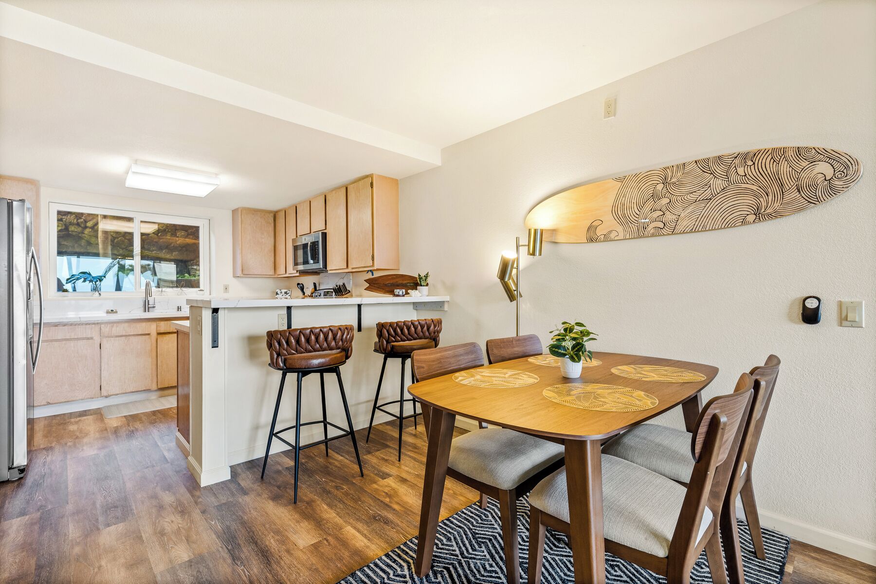 A compact kitchen with wooden cabinets, a microwave, and a small island. There is a dining area with a wooden table and four chairs.