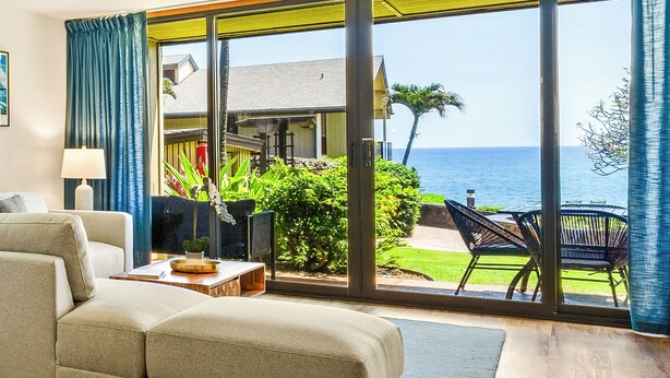Uma sala de estar espaçosa com uma grande porta de vidro deslizante que dá para uma varanda com vista para o oceano.