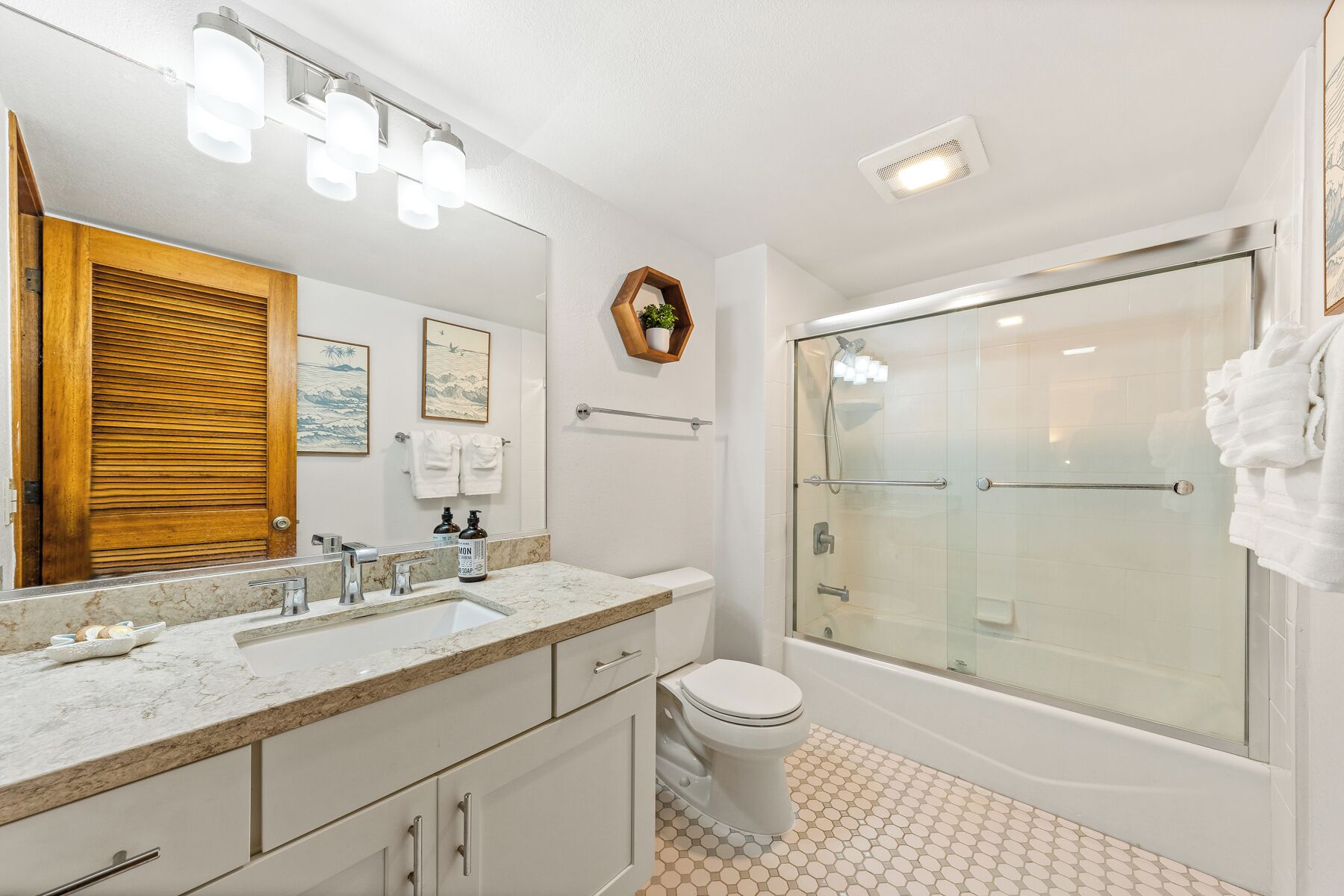 Un baño moderno con un espejo grande, un lavamanos con encimera de mármol, un inodoro y una zona de ducha con mampara de cristal.