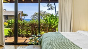 Quarto com porta de correr de vidro que dá para uma varanda com vista para o oceano e vegetação tropical.