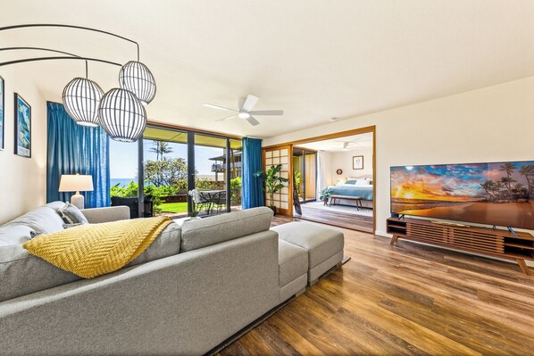 A modern living room with a grey sofa, a yellow throw blanket, and a large flat-screen TV. - Makahuena 2106 (Koloa)
