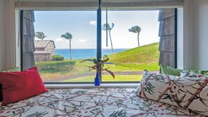 Ein Schlafzimmer mit einem Bett, das zu einem Fenster mit Blick auf eine Rasenfläche und Palmen führt, mit Meerblick.