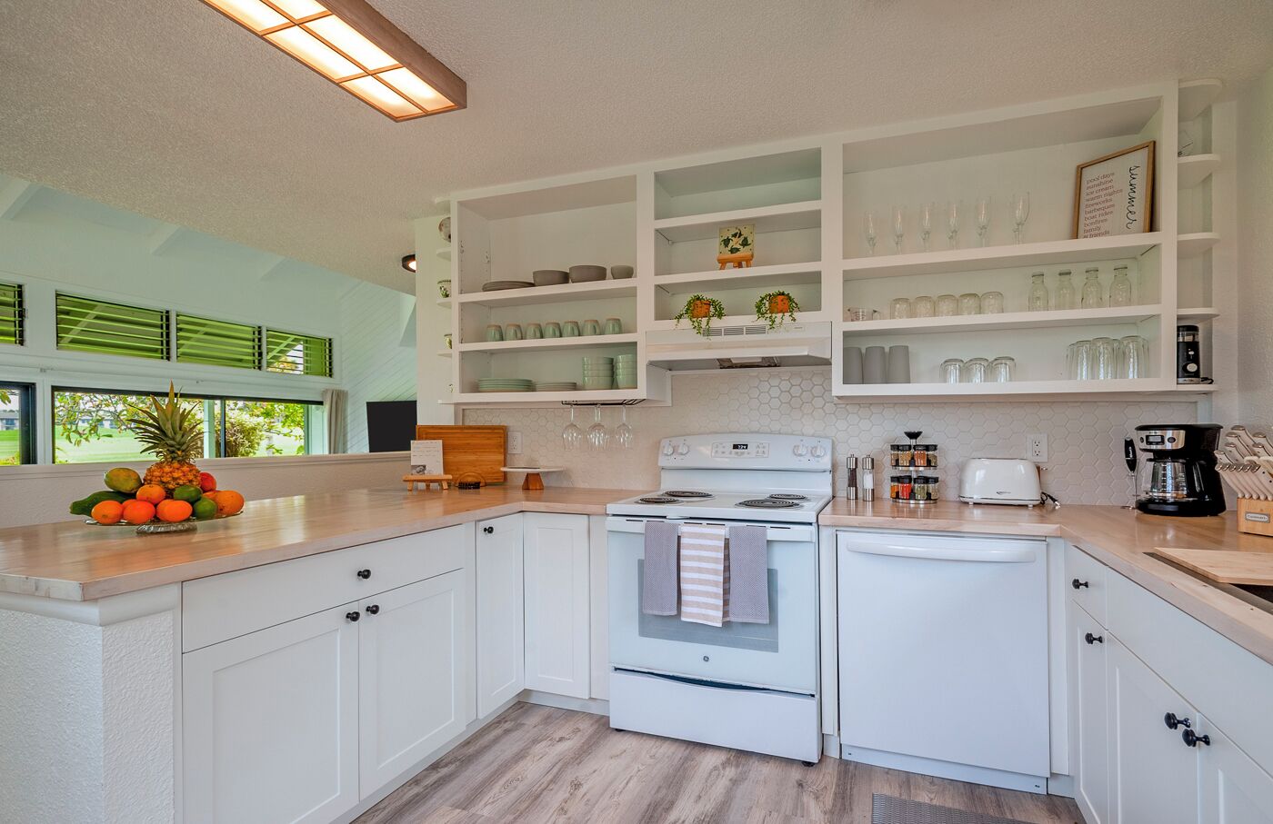 Een moderne keuken met witte kasten, een centraal eiland en uitzicht op de omgeving door grote ramen.