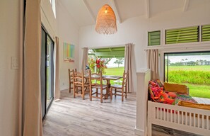 Une pièce comprenant une table à manger et des chaises, un lit avec une literie aux couleurs vives, un luminaire suspendu et une vue sur un champ verdoyant par la fenêtre.