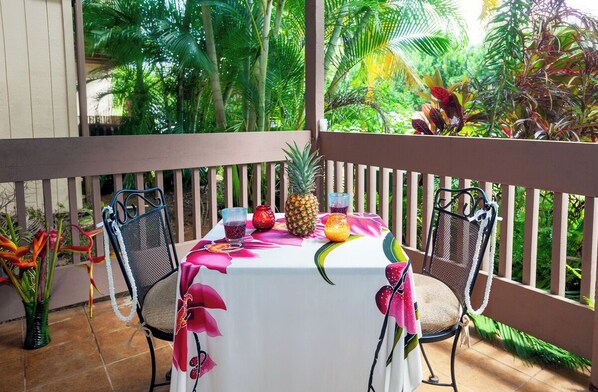 Ein Tisch auf einem Balkon mit weißer Tischdecke, zwei Stühle, einer Ananas und verschiedenen Getränken.