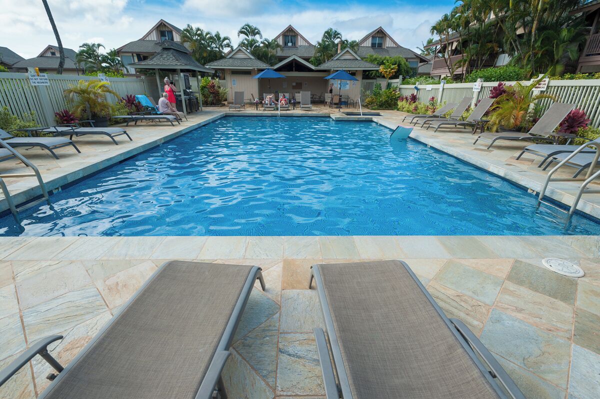 A swimming pool with lounge chairs and umbrellas, surrounded by houses and palm trees.