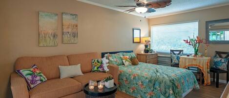 A cozy bedroom with a bed, a sofa, a small table with candles, and a ceiling fan.