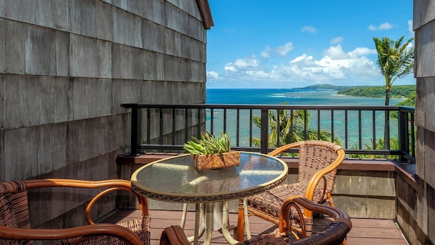 A balcony with wicker furniture, a glass table, and a potted plant. - Sealodge E10 (Princeville)