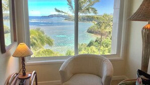A room with a large window offering a view of a tropical beach and ocean. - Sealodge E10 (Princeville)