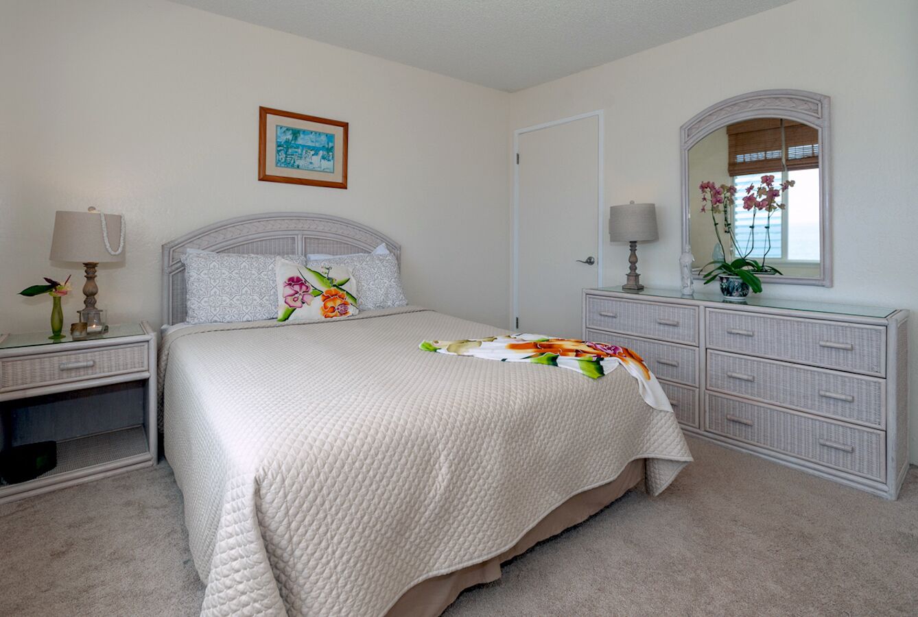 A bedroom with a bed, nightstands, a dresser, a mirror, and a framed picture on the wall.