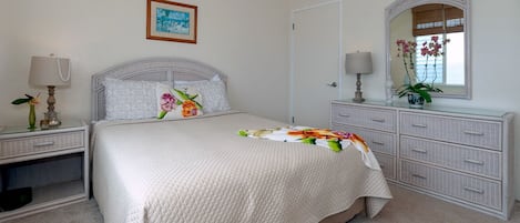 Ein Schlafzimmer mit Bett, Nachttischen, einem Schminktisch und einem Spiegel, sowie einem gerahmten Bild an der Wand.