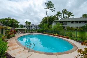 A swimming pool with a curved edge, surrounded by a stone deck and a metal fence. - Alii Kai 3103 (Princeville)