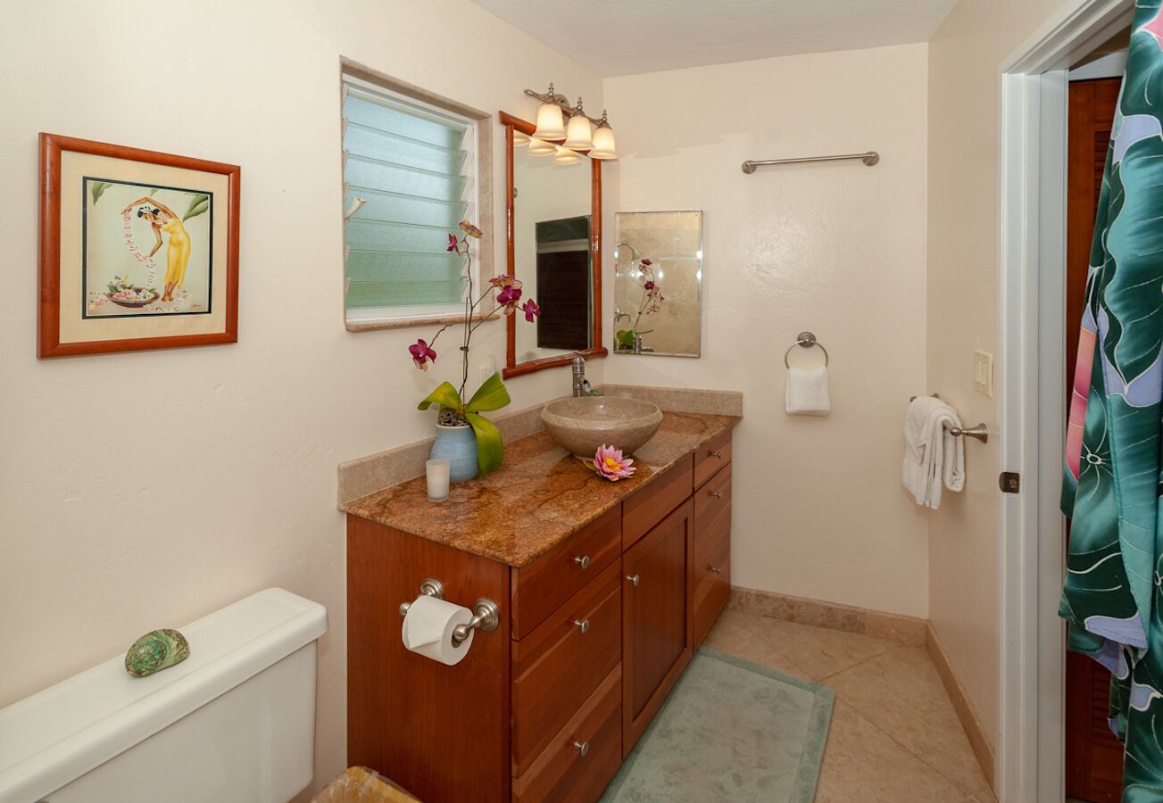 A bathroom with a wooden vanity, a sink with a mirror, a toilet, and a shower curtain.
