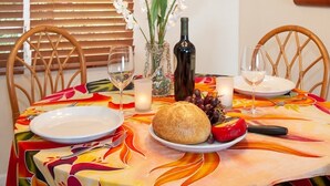 Et spisebord med en farverig dug, et brød, en vinflaske og en vase med blomster.