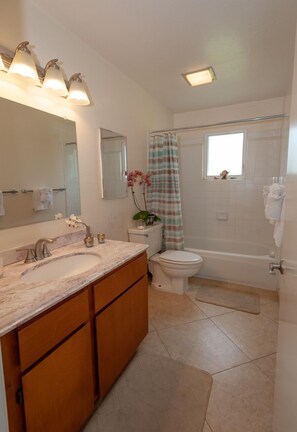 A bathroom with a marble sink, wooden cabinets, a toilet, a bathtub, and a shower curtain. - Alii Kai 3103 (Princeville)
