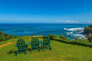 A grassy area with three green Adirondack chairs facing a view of the ocean. - Alii Kai 3103 (Princeville)