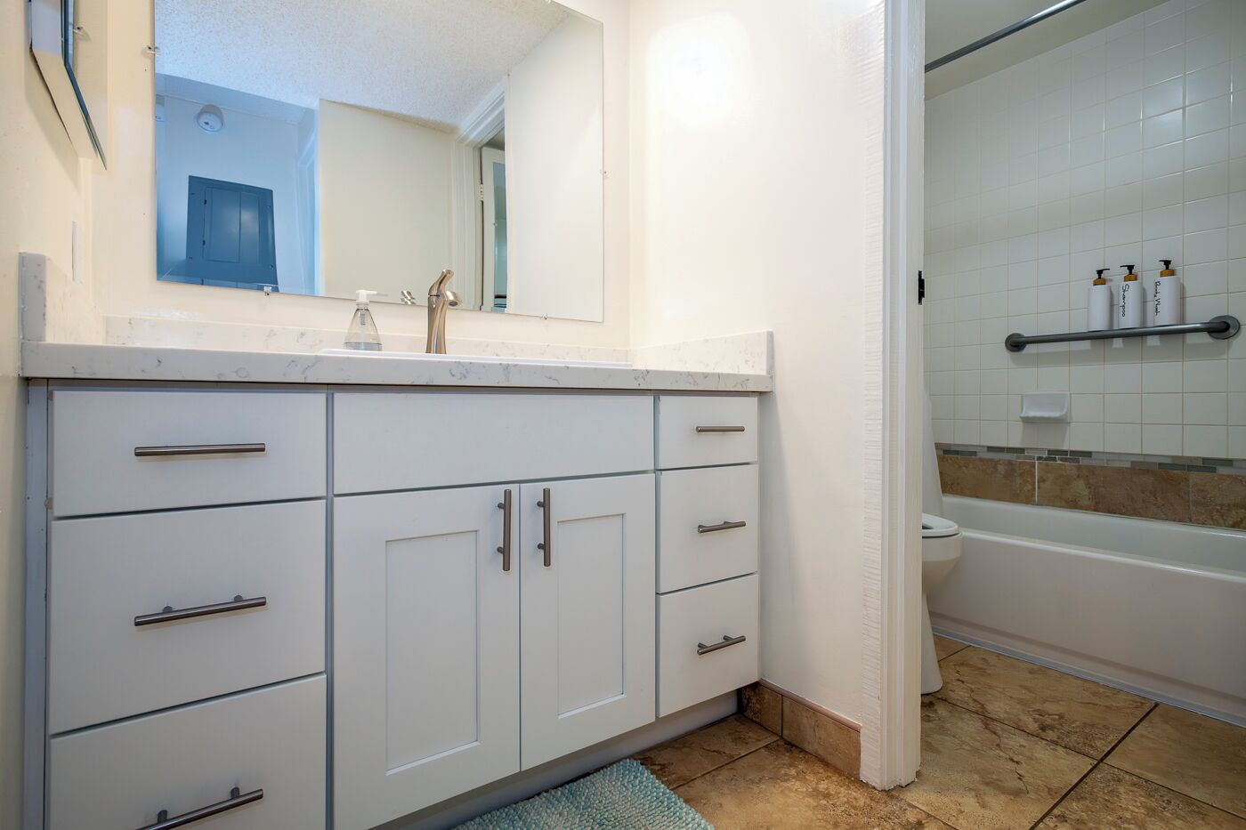 A bathroom with a white sink, mirror, and cabinet. There is a bathtub with a shower curtain and toiletries on a shelf.