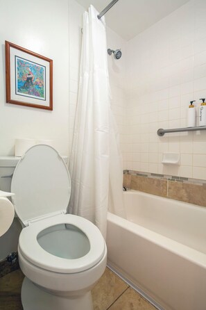 A bathroom with a toilet, a shower curtain, a bathtub, and a shelf with toiletries.