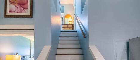 Una escalera con peldaños blancos y barandillas de madera que conduce a un rellano con una lámpara y un espejo.