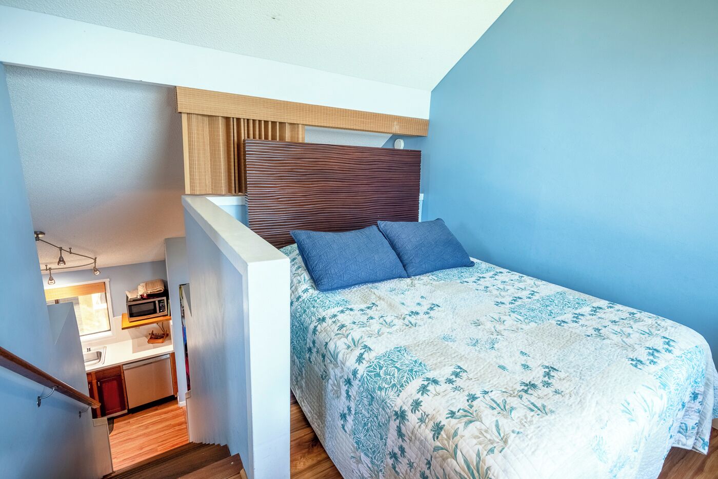 A compact bedroom with a bed, a small kitchenette, and a wooden staircase.