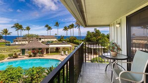 Un balcon donnant sur une piscine, des palmiers et un bâtiment au toit de chaume.