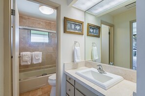 Un baño con ducha de vidrio, un lavamanos blanco y dos cuadros en la pared.