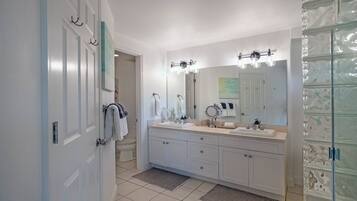 Un baño moderno con un tocador grande, dos lavamanos, un espejo y una cabina de ducha de vidrio.