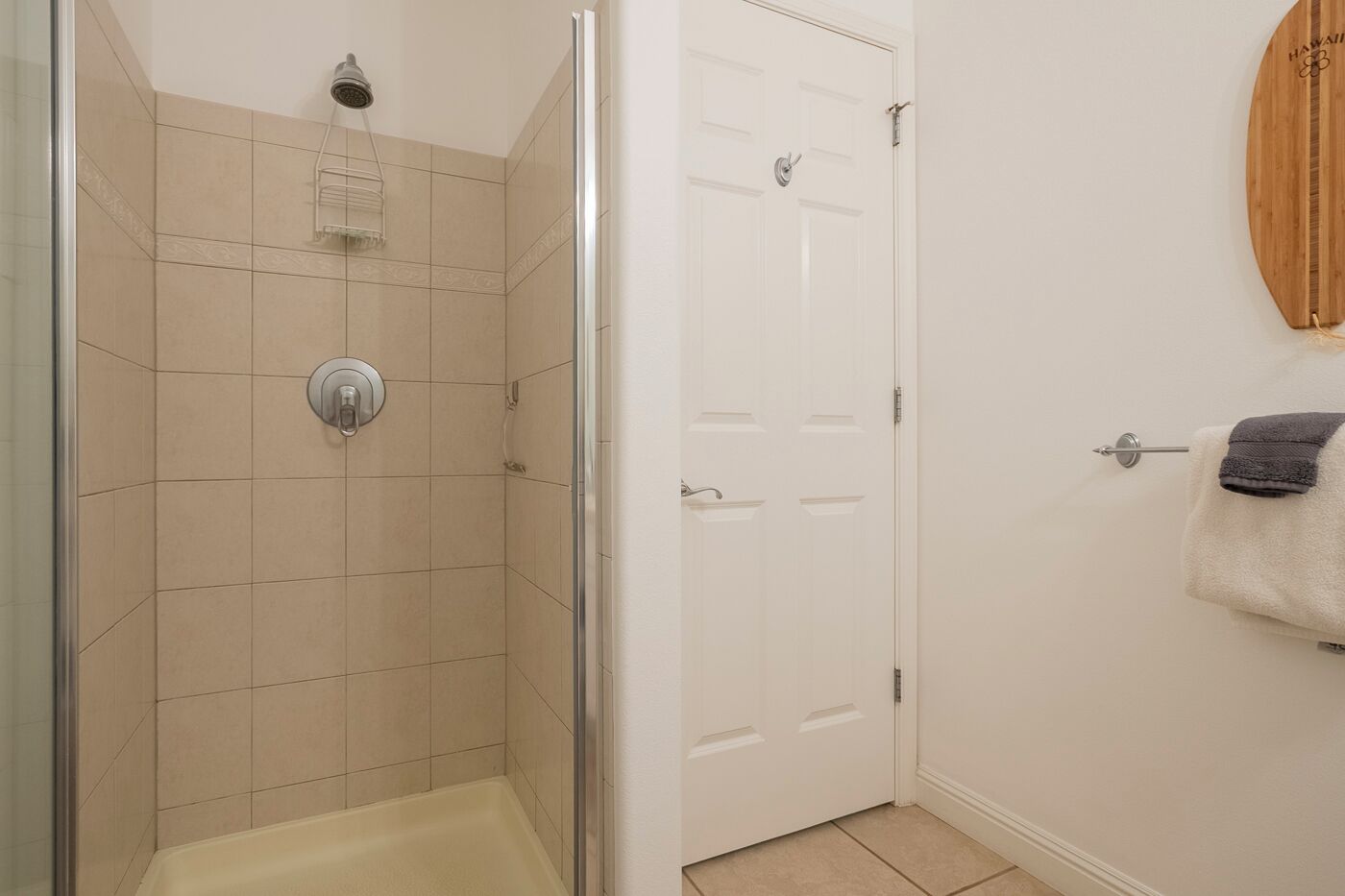 A bathroom with a glass shower enclosure, a bathtub, and a white door with a towel hanging on the wall.