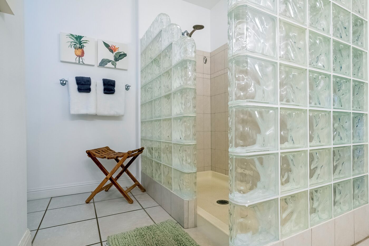 Un baño con mampara de vidrio, una silla plegable de madera y dos toallas colgadas en la pared.