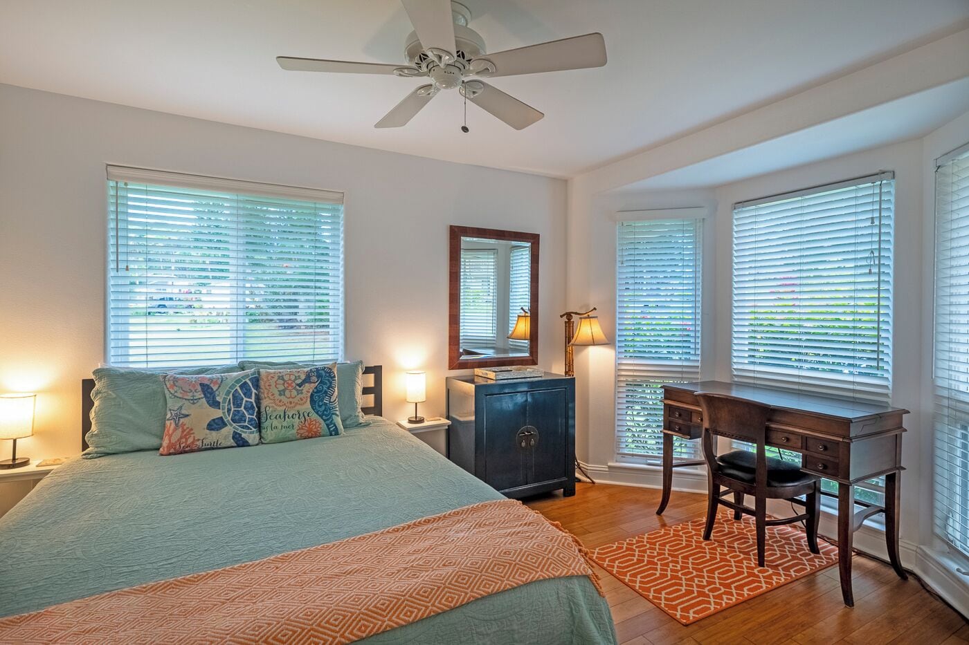 A bedroom with a bed, desk, chair, dresser, and a ceiling fan.