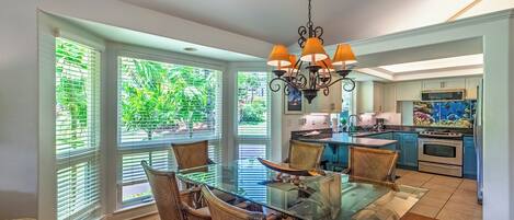 A modern kitchen with a central island, large windows, and a dining area with wicker chairs and a glass table.