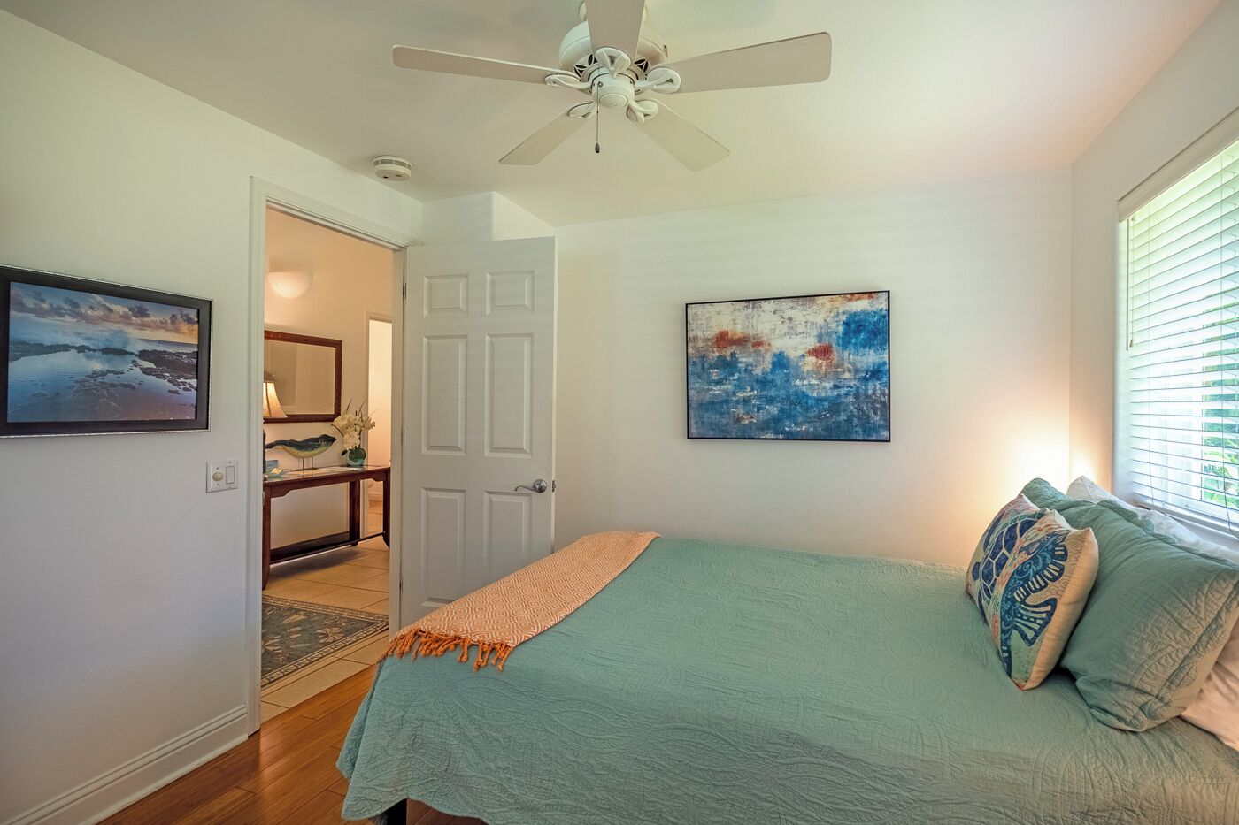 Une chambre à coucher avec un lit, un ventilateur de plafond, une porte et deux œuvres d’art encadrées accrochées au mur.